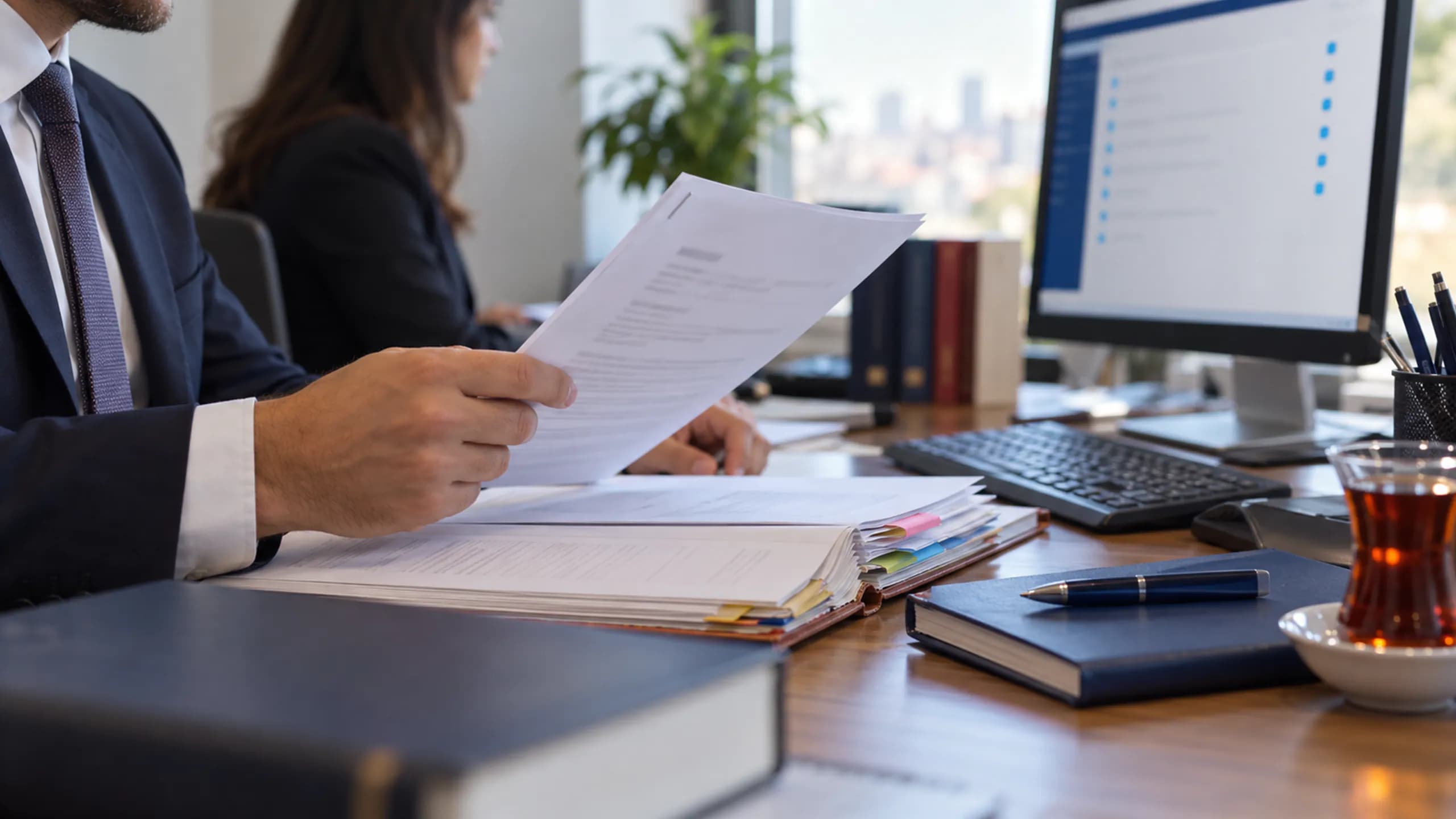 Avukat büro masasında elektronik dava dosyasını incelerken yanında fiziksel dosya açık duruyor; UYAP entegrasyonu rehberi için editoryal fotoğraf